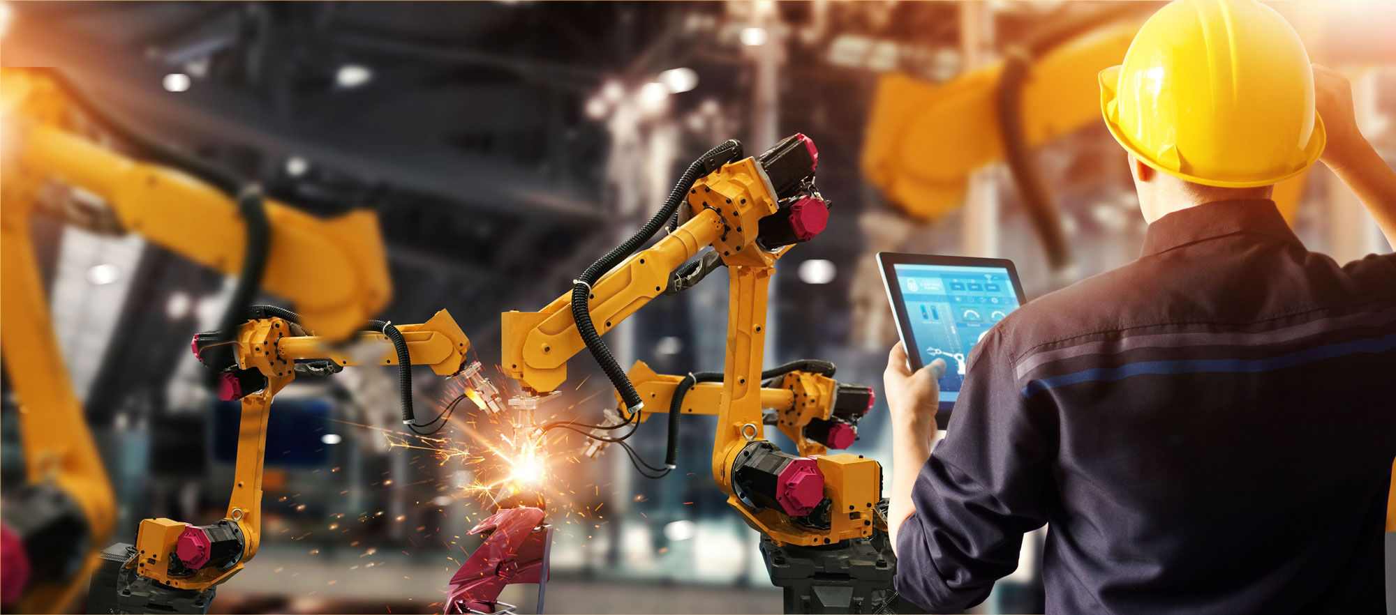 Engineer with tablet monitoring robotic welding arms on a factory floor