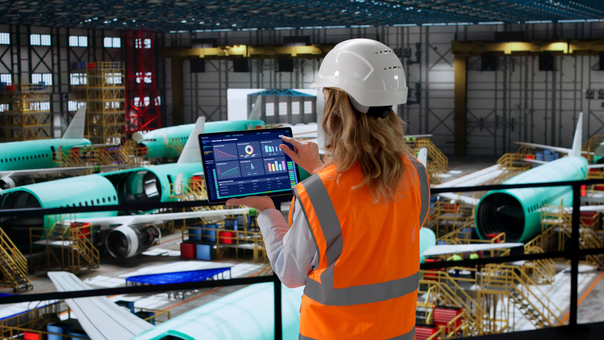 Aerospace engineer using OpX OS analytics on a tablet inside an aircraft assembly hangar
